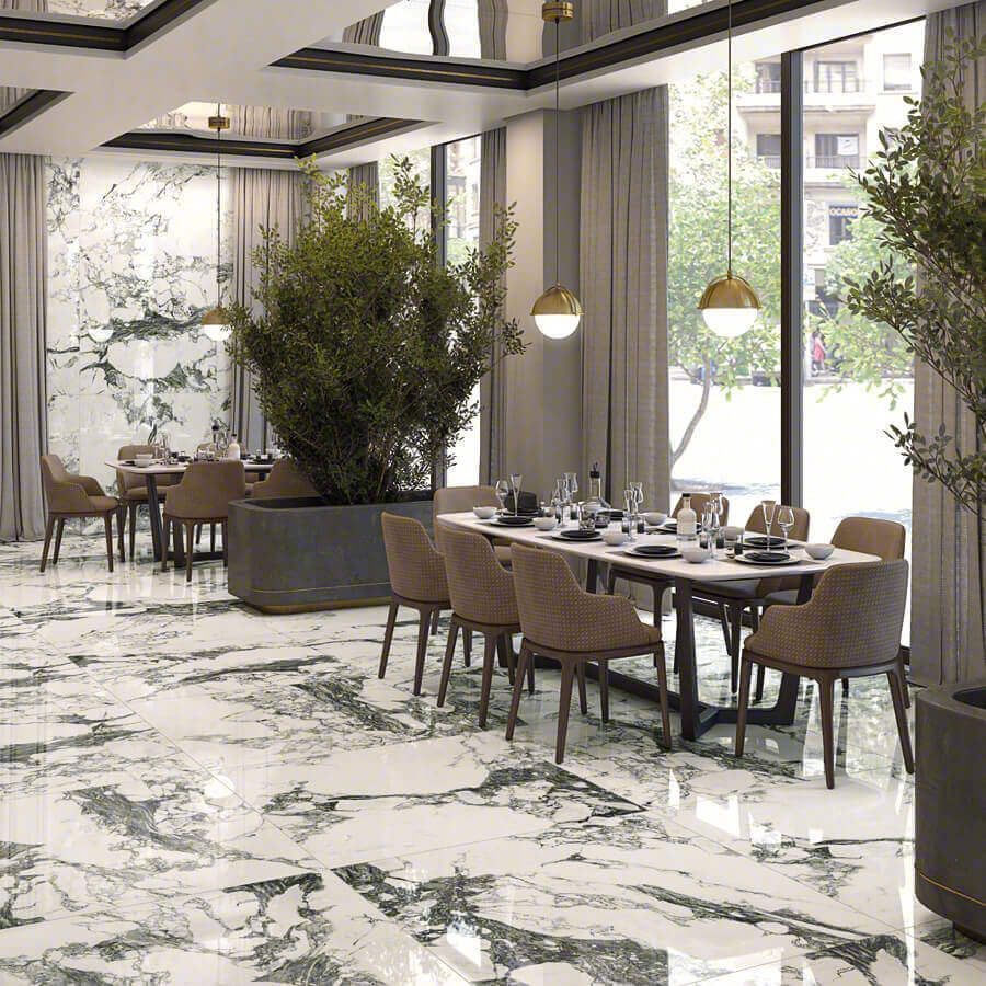 Elegante interior de restaurante con pisos y paredes de mármol, mesas preparadas para comer y grandes plantas en macetas.