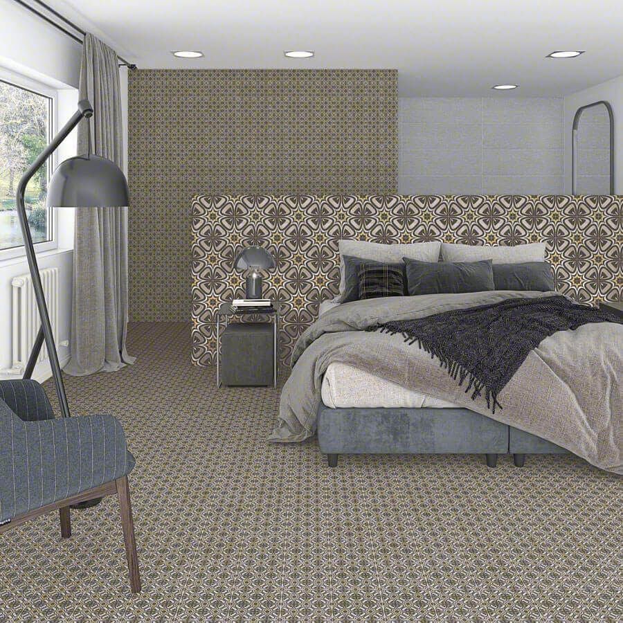 Dormitorio con papel pintado estampado detrás de una cama. Ropa de cama gris, alfombra estampada, silla y lámpara.