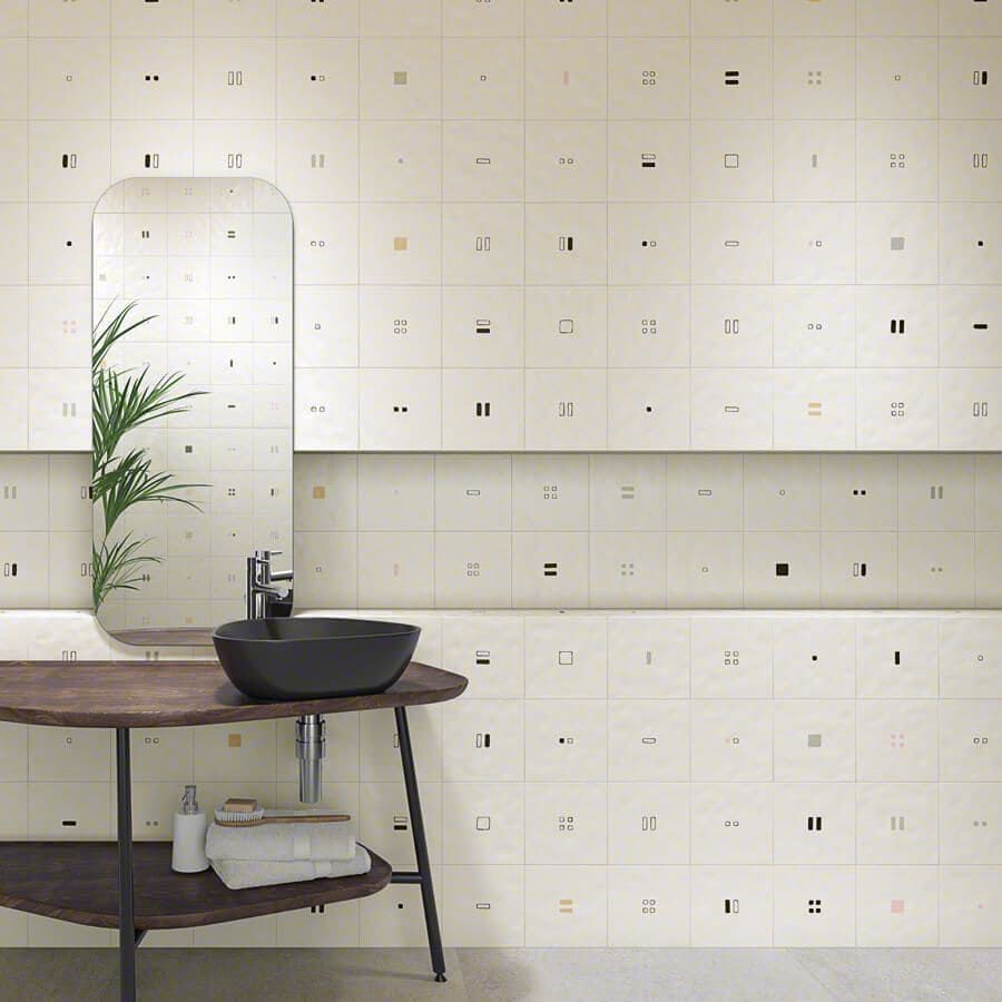 Baño con pared de azulejos geométricos color crema y tocador de madera. Lavabo, espejo y planta negros.