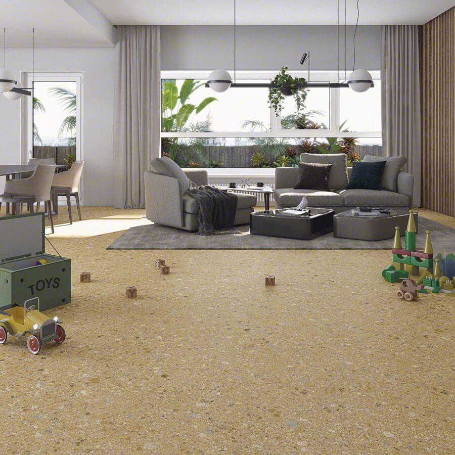 Sala de estar con suelo de terrazo amarillo, juguetes esparcidos, zona de estar, ventana con plantas.