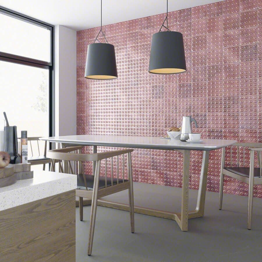 Comedor con pared texturizada rosa, mesa moderna, lámparas colgantes grises y sillas de madera clara.