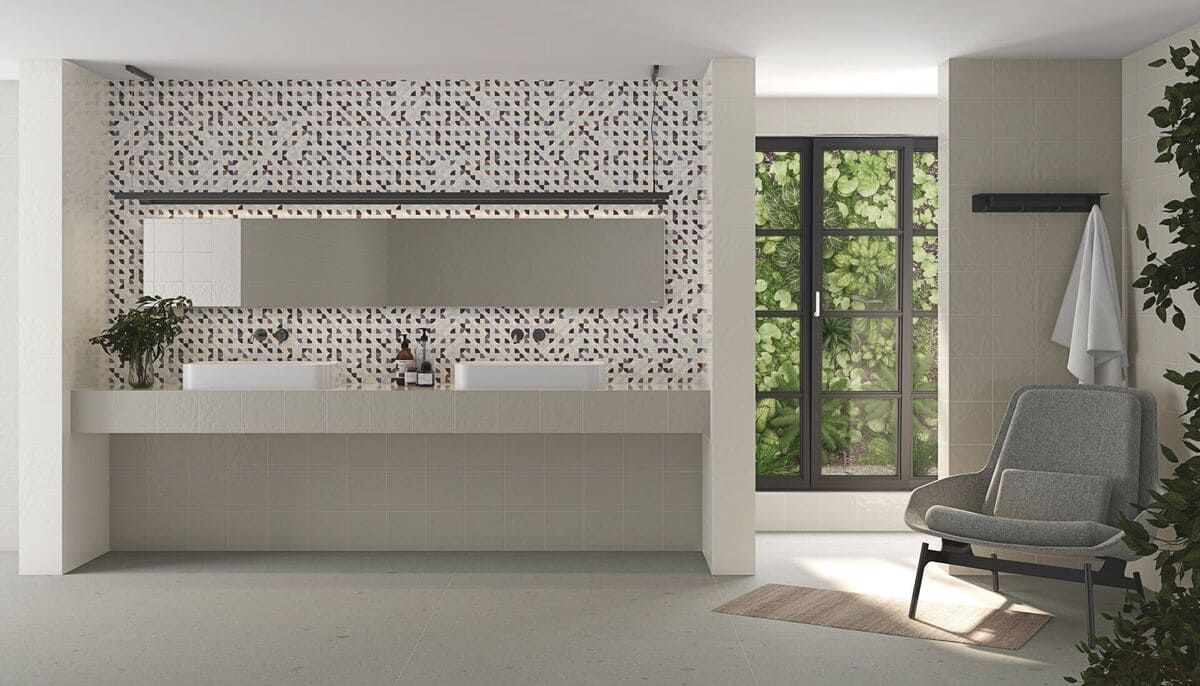 Baño moderno con lavabo doble, azulejos de pared estampados, ventana con vegetación y un sillón.