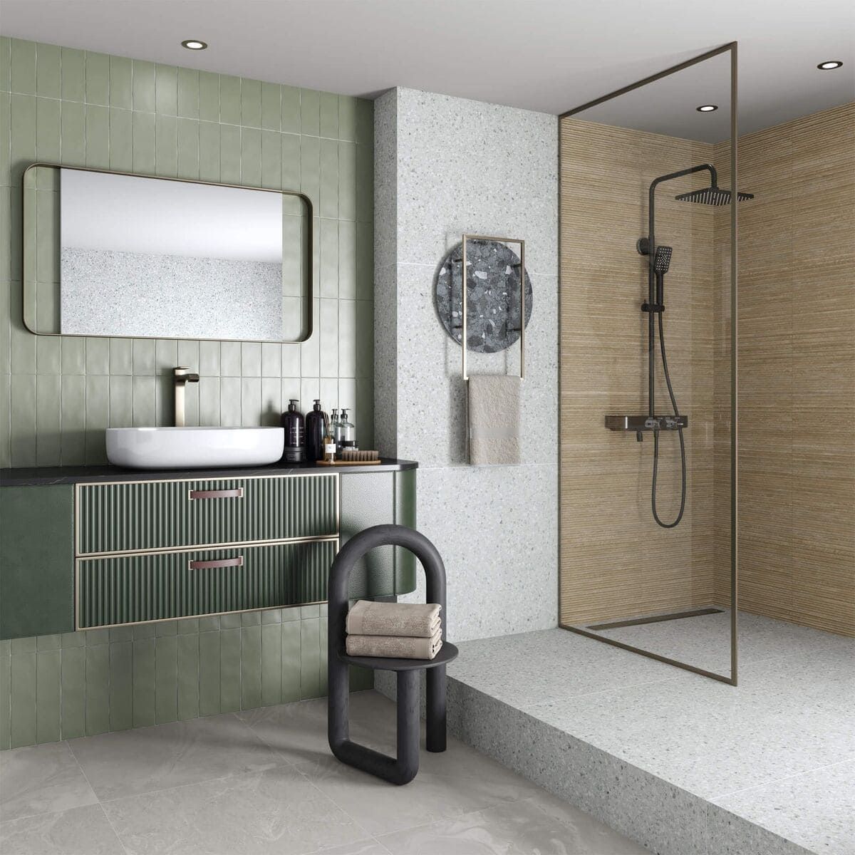Baño moderno con azulejos verdes y beige, ducha, tocador y silla negra.