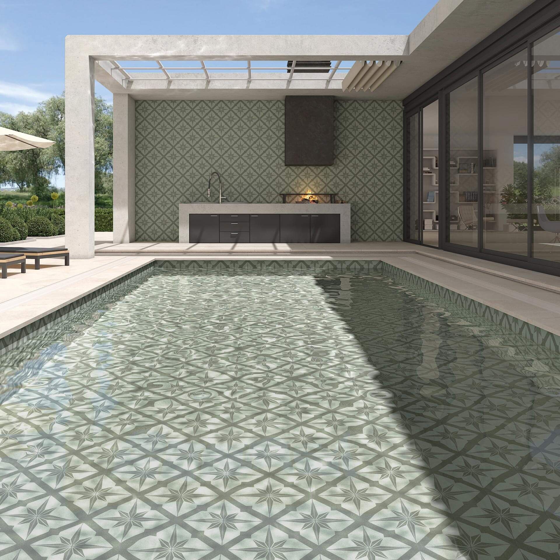 Piscina con azulejos decorativos, cocina exterior y pérgola en entorno soleado.