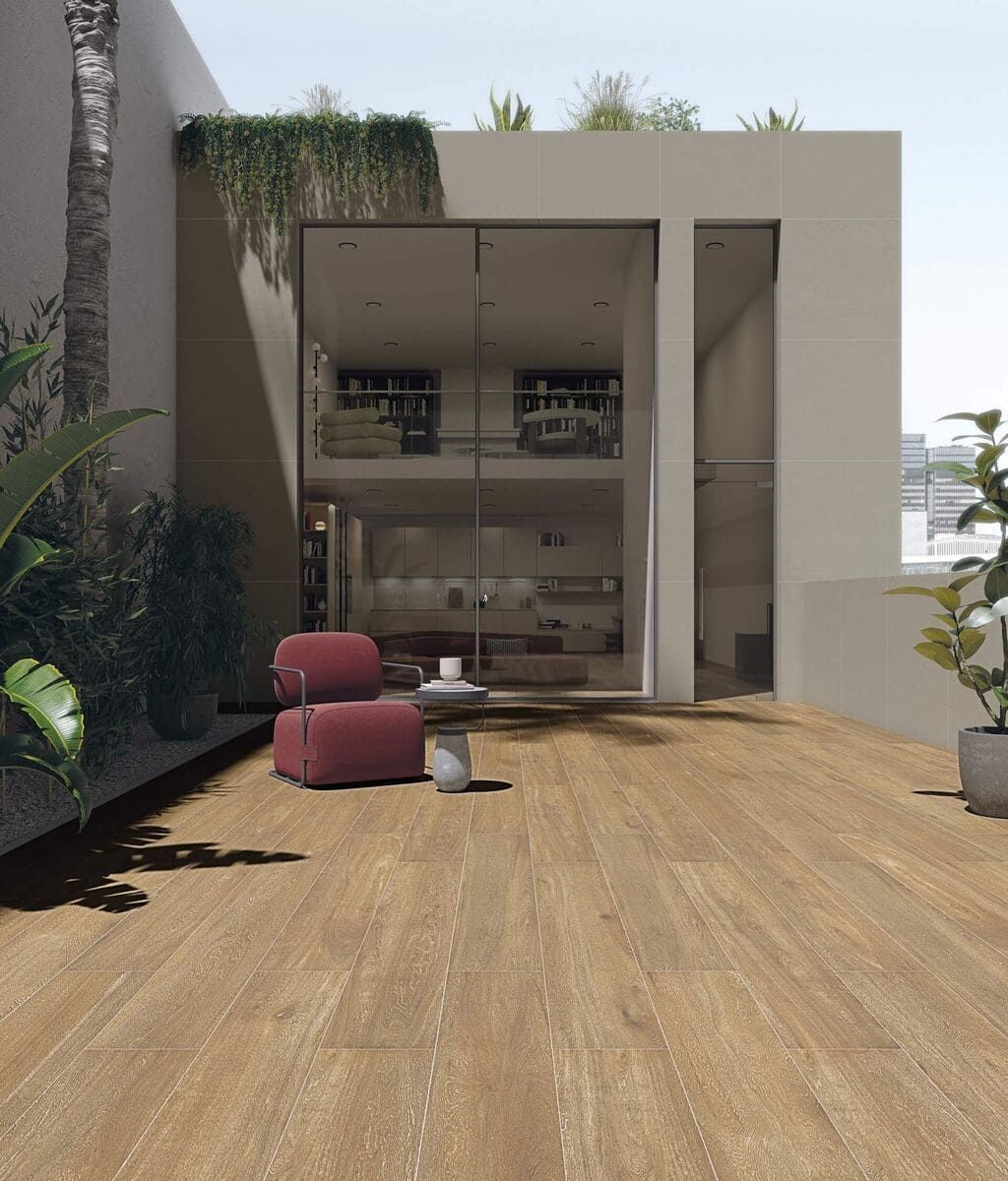 Patio exterior con baldosas imitación madera, sillones rojos, estructura con paredes de vidrio y vegetación.