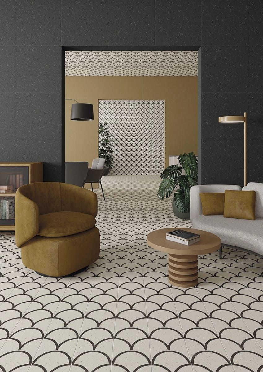 Sala de estar con piso de baldosas estampadas, silla de terciopelo y sofá, que se abre a otra habitación con pared estampada.