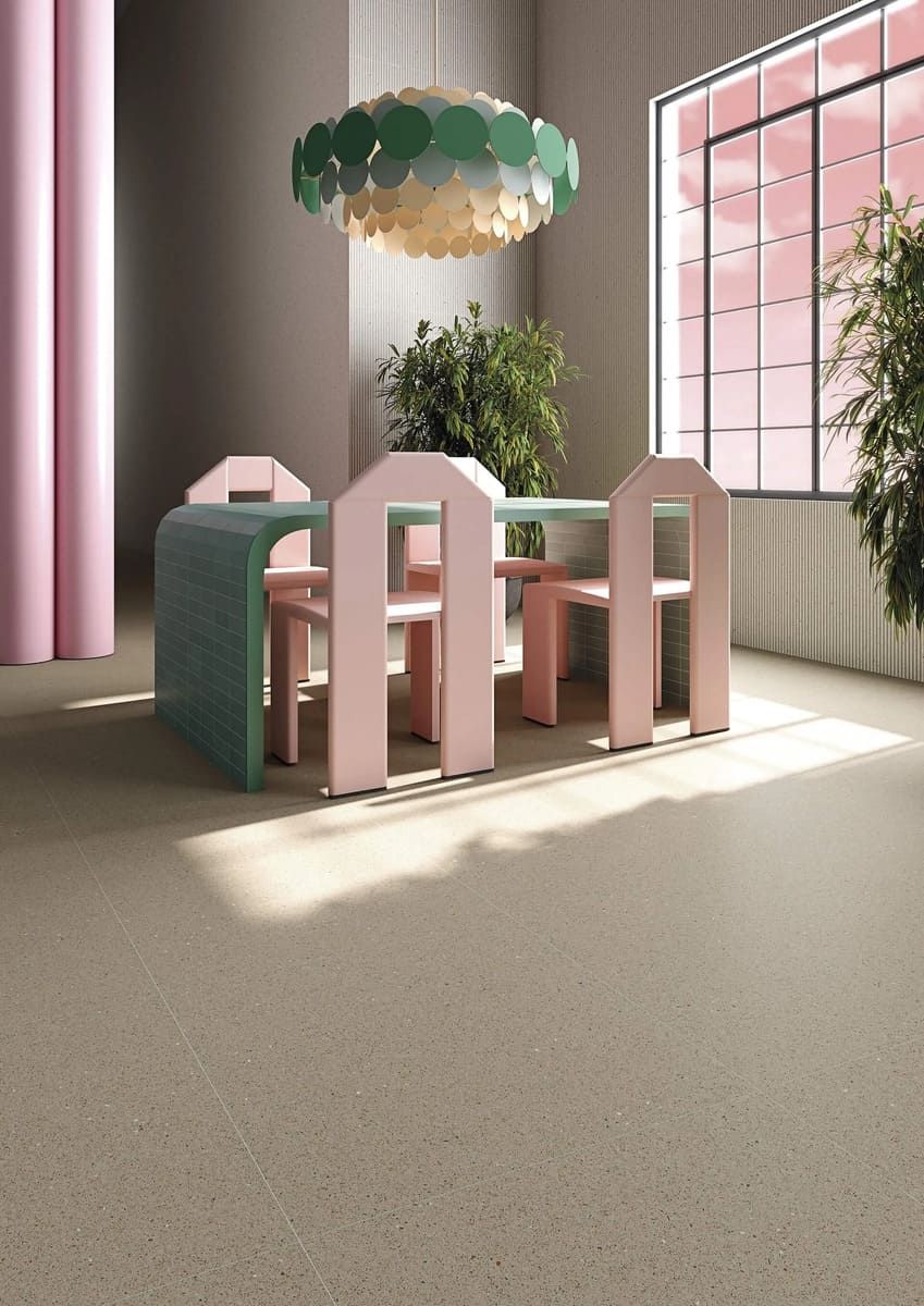 Una habitación caprichosa con una mesa rosa y verde. Suelo beige suave y una gran ventana con luz rosa.