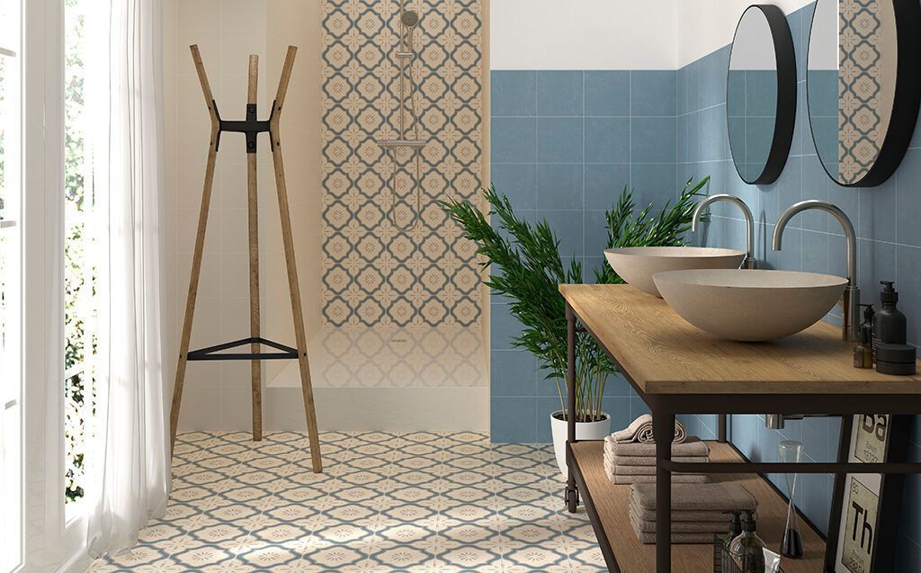 Baño con piso de baldosas estampadas, pared azul, tocador de madera con lavabos y perchero.