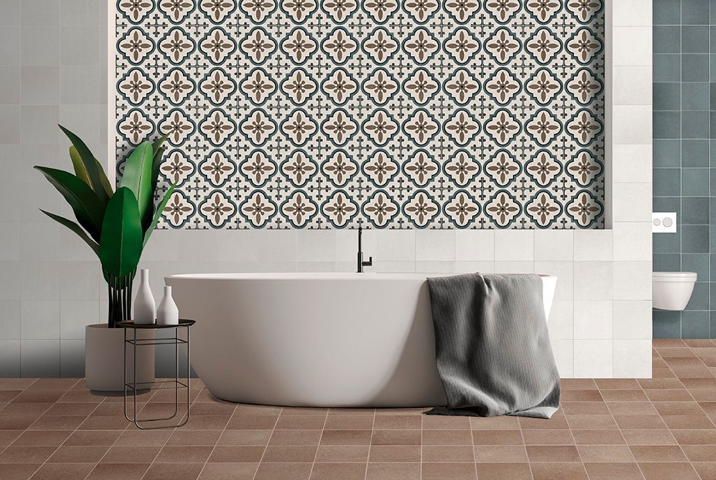 Baño con una pared con acento de azulejos estampados, bañera blanca y plantas sobre un piso de baldosas marrones.