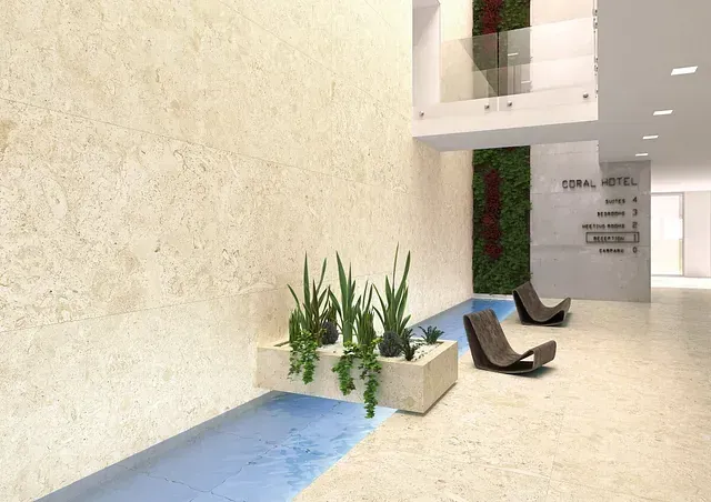 Vestíbulo de hotel con paredes de piedra, plantas y asientos modernos. Fuente de agua. Señales de dirección en la pared.