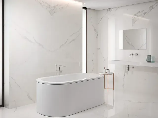 Baño blanco moderno con bañera independiente, paredes de mármol y tocador minimalista.