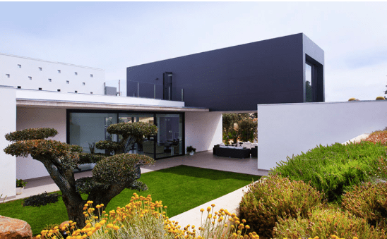 Casa moderna con sección superior negra y sección inferior blanca, que cuenta con un patio con césped verde y paisajismo.