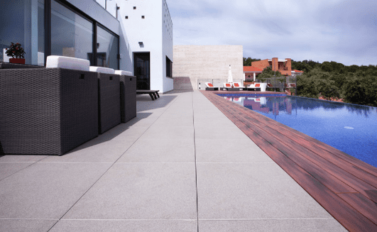 Patio con piscina, edificio blanco moderno y muebles oscuros. Agua de la piscina azul.