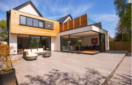Casa moderna con fachada de madera, amplio patio y sala de estar diáfana bajo un cielo azul.