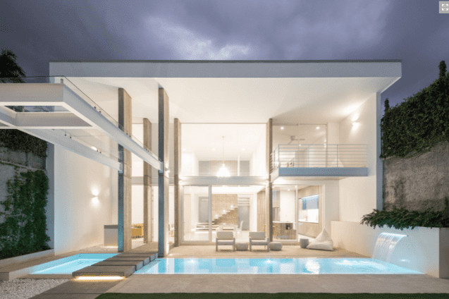 Casa blanca moderna con piscina, paredes de cristal y terraza. Iluminación nocturna.