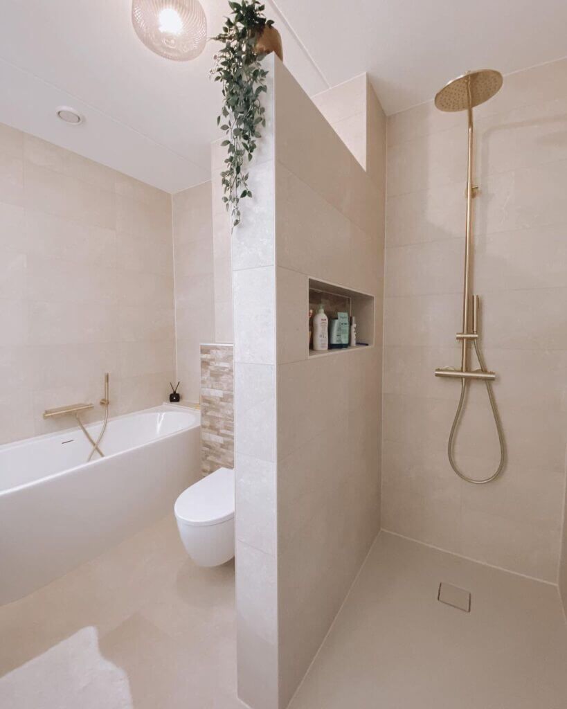 Baño moderno de color beige con bañera profunda, inodoro y ducha con accesorios dorados.
