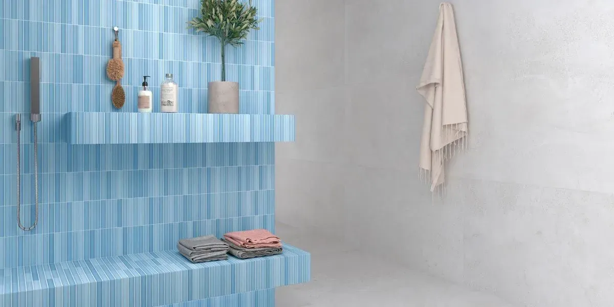 Una ducha con azulejos azules con un estante que contiene artículos de tocador y una planta en maceta; una toalla cuelga en la pared adyacente.