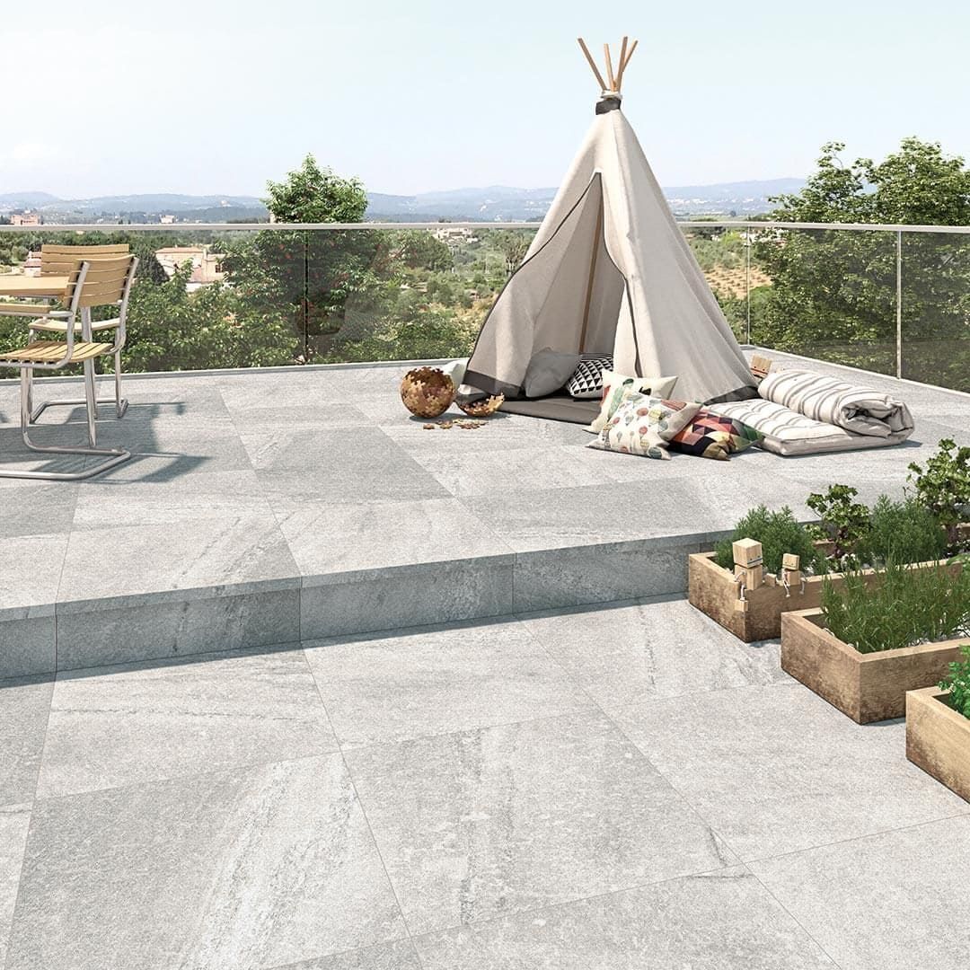 Patio de piedra gris con tipi, parterres y paisaje urbano al fondo.