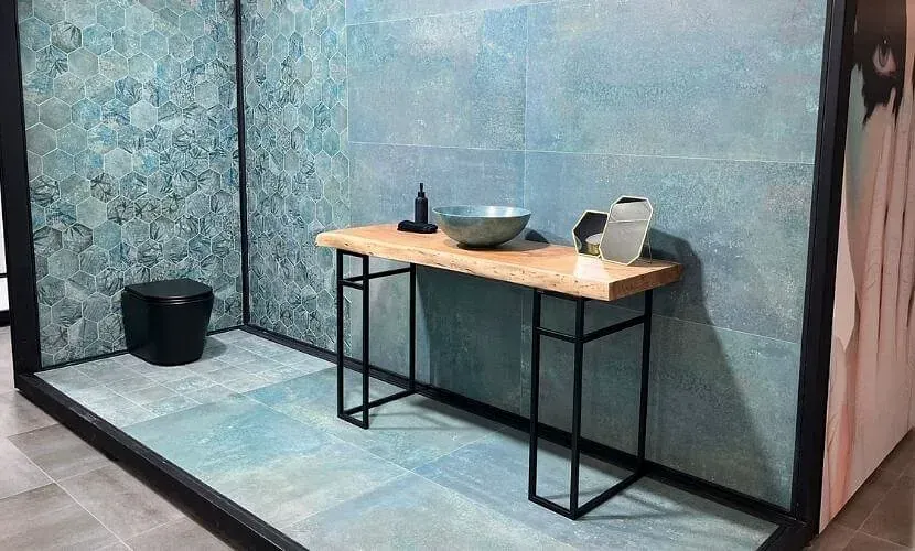 Exhibición de baño con azulejos de color azul verdoso, consola de madera y accesorios negros.