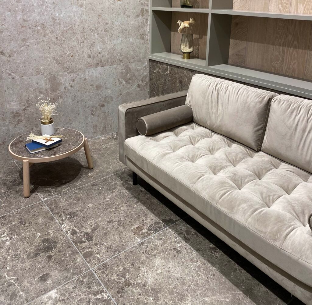 Acogedora sala de estar con sofá capitoné, mesa redonda y estanterías empotradas. Combinación de colores gris y tostado.