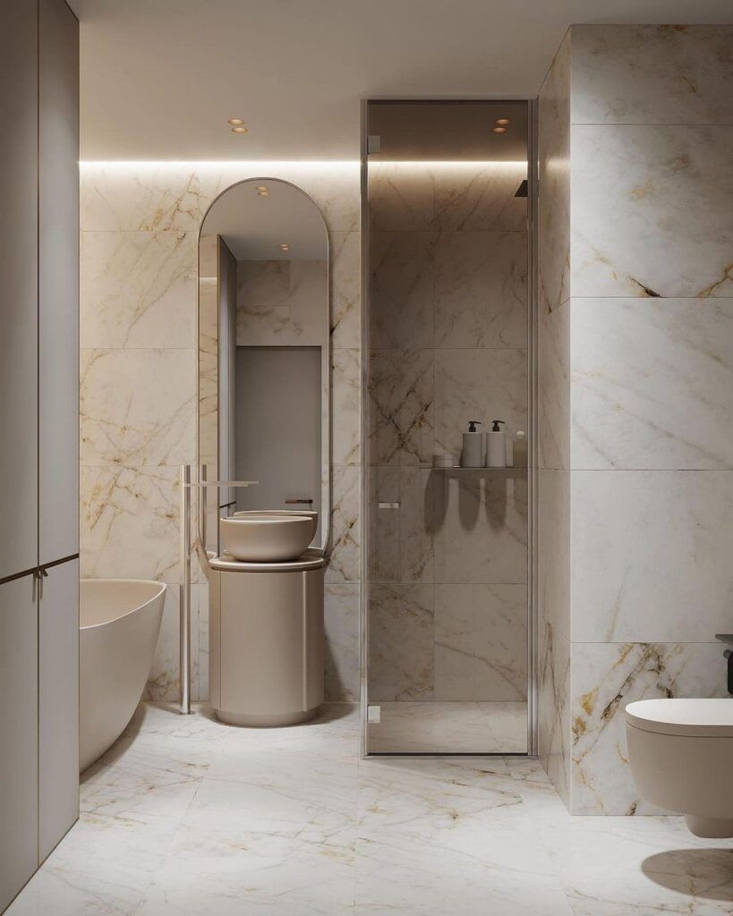 Elegante baño con paredes de mármol, ducha, lavabo e inodoro en tonos beige.