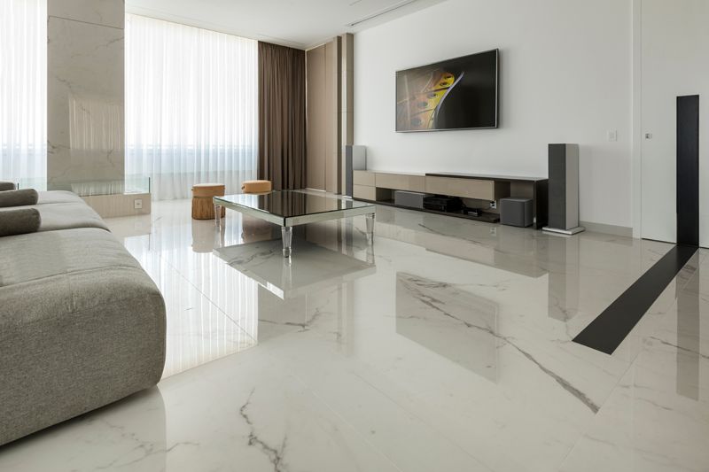 Moderna sala de estar con pisos de mármol, sofá gris, TV y gran ventanal con cortinas.