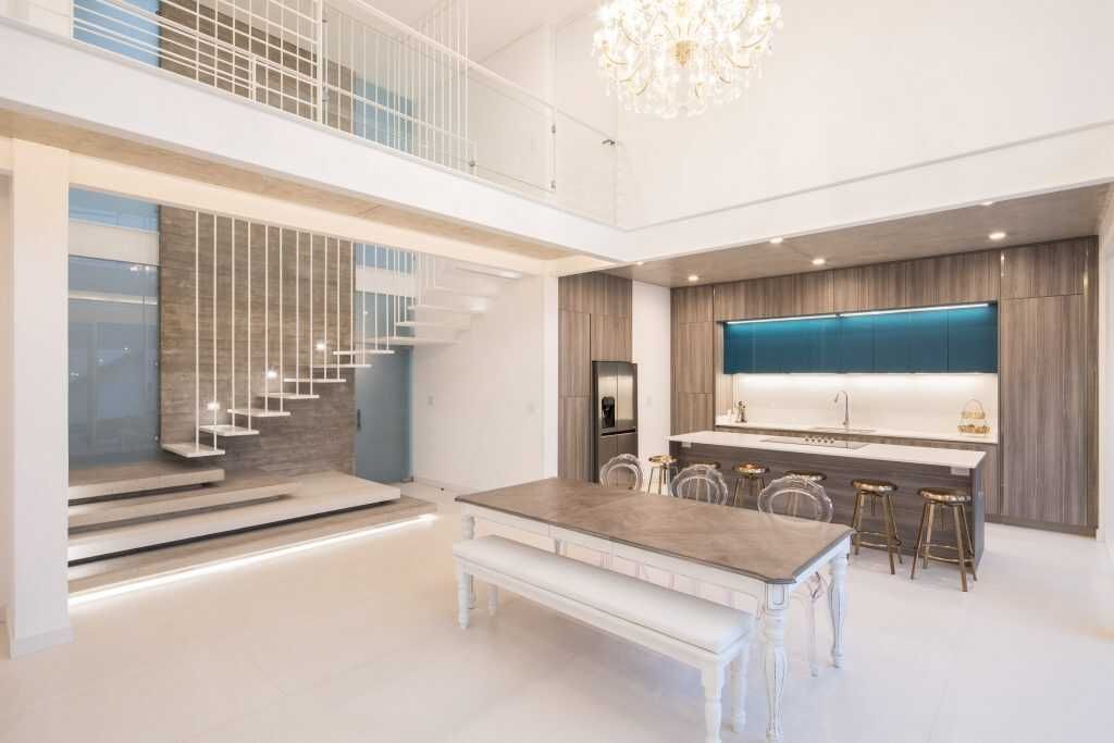 Cocina moderna con techo alto, mesa de comedor y escalera que conduce a un loft.