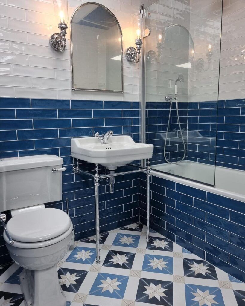 Baño con azulejos azules y blancos, lavabo de pedestal, inodoro y bañera.