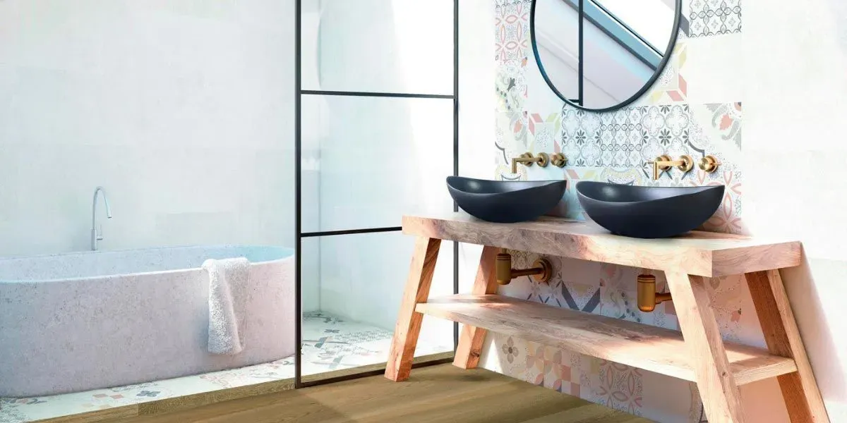 Baño con lavabo de madera, lavabos negros y espejo redondo. Al fondo se ve una bañera.