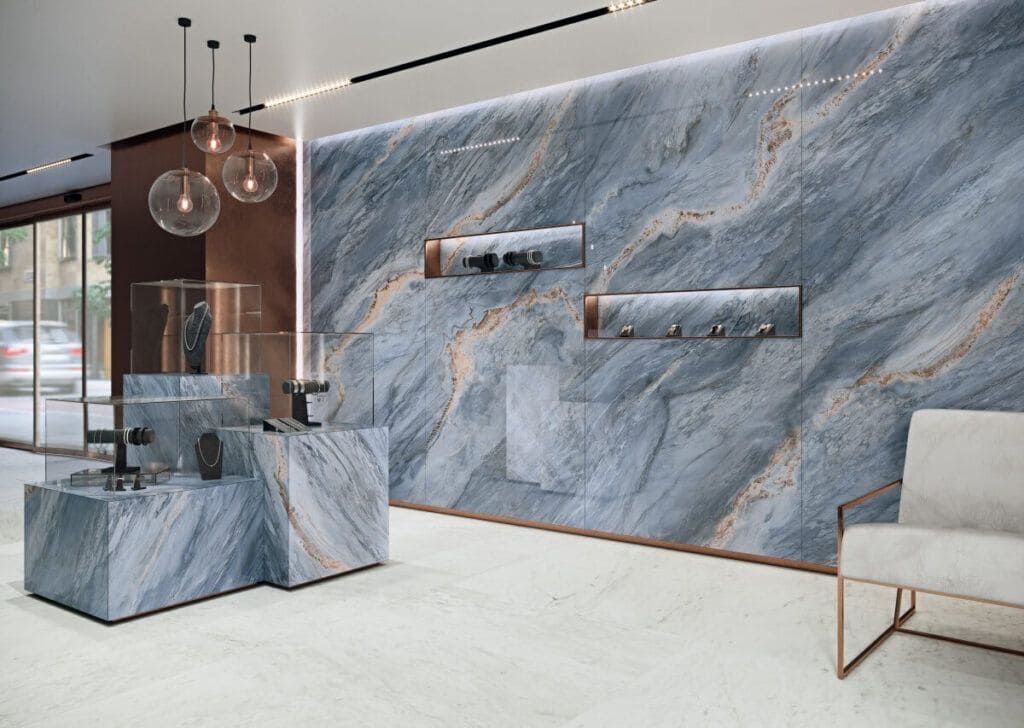 Interior de joyería de lujo con pared de mármol azul y mesas de exhibición; iluminación moderna.