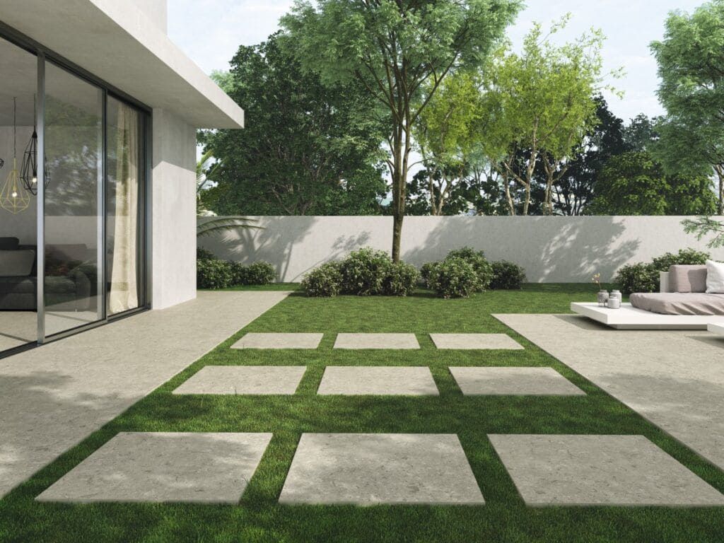 Un patio trasero moderno con césped, adoquines de piedra y una casa blanca con puertas corredizas de vidrio.