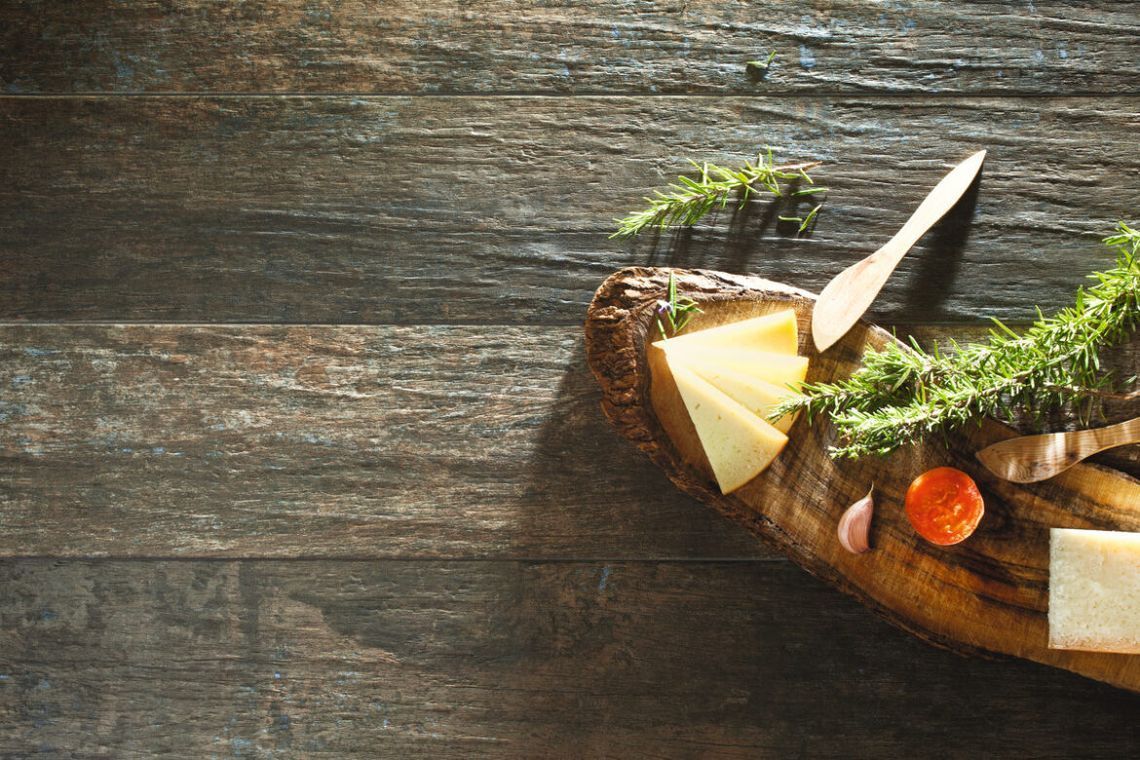 Lonchas de queso, hierbas y tomate sobre tabla de madera. Fondo rústico de mesa de madera.