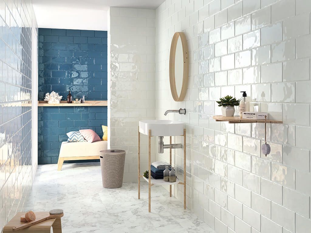 Baño con paredes de azulejos blancos, lavabo, espejo y una zona de azulejos azules con marco de cama.