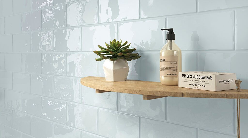 Pared de azulejos de color azul claro con un estante de madera que sostiene una suculenta, un dispensador de jabón y una pastilla de jabón.