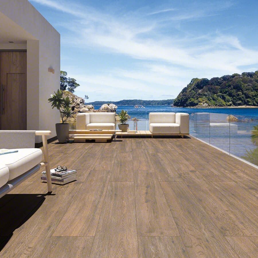 Terraza de madera con vistas al océano azul y a la isla, con muebles blancos.