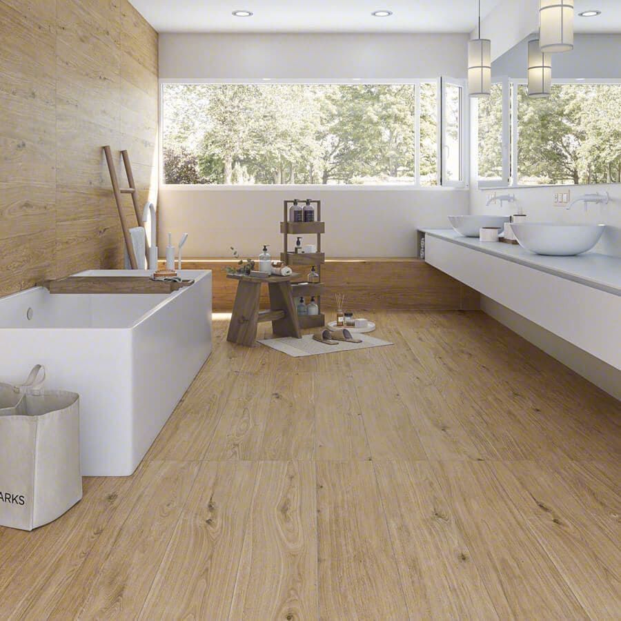 Un baño moderno con suelos de madera, bañera blanca y grandes ventanales con vistas a los árboles.