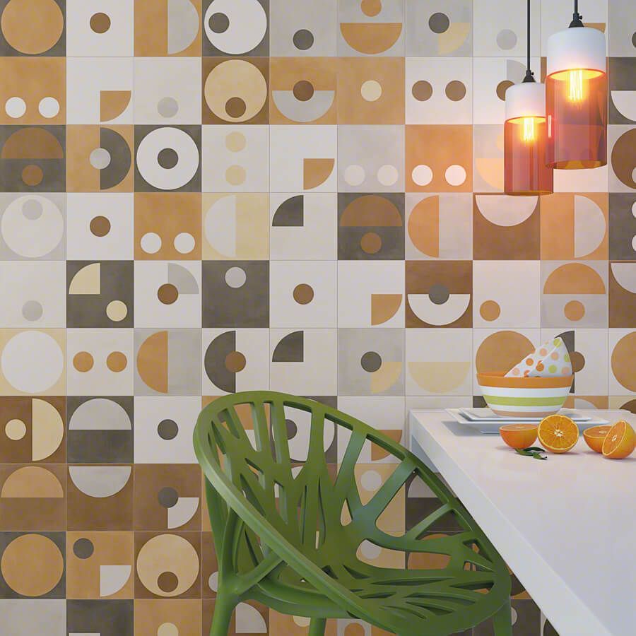 Pared de azulejos geométricos con silla verde, encimera blanca y lámparas colgantes. Naranjas y un cuenco.