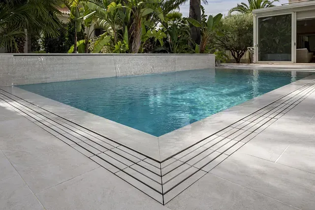 Una piscina rectangular de agua turquesa cristalina, rodeada de azulejos blancos. Con exuberante vegetación al fondo.