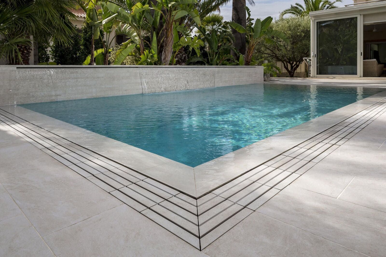Una piscina rectangular de agua turquesa, rodeada de piedras de color claro y vegetación.