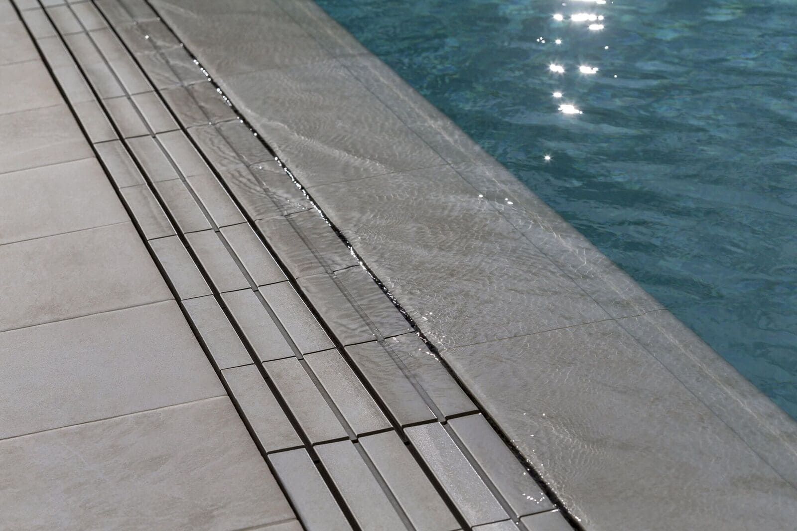 Borde de piscina con borde de baldosas, agua que desborda hacia una rejilla.