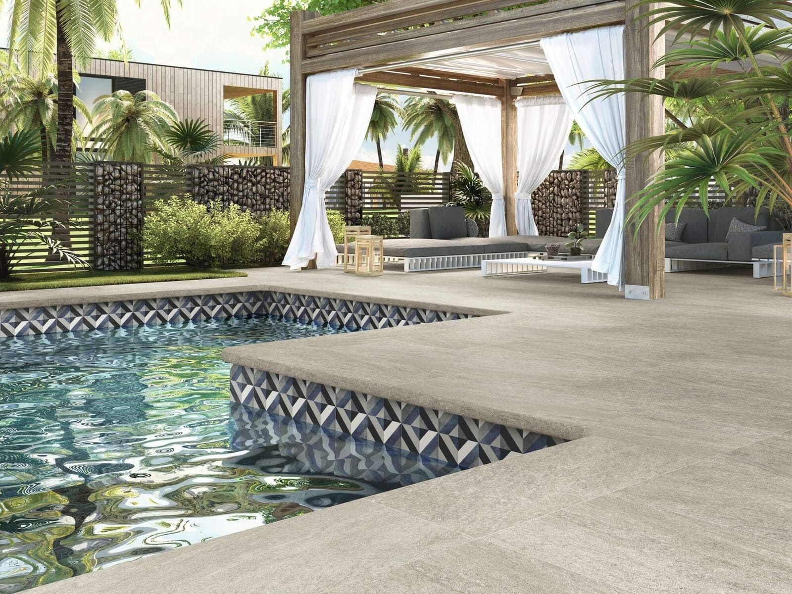 Piscina con borde de azulejos estampados, patio de colores claros y una zona de estar a la sombra con cortinas blancas.