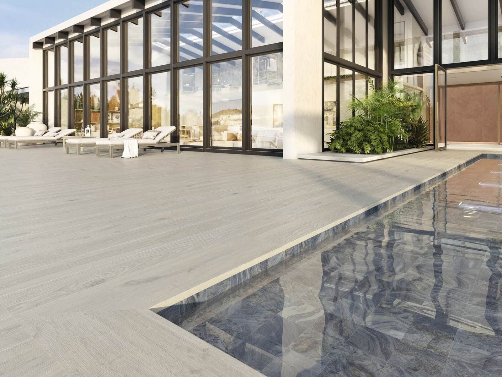 Una moderna piscina en la azotea con un edificio de grandes ventanales. Un patio de piedra gris y el agua reflejan el cielo.