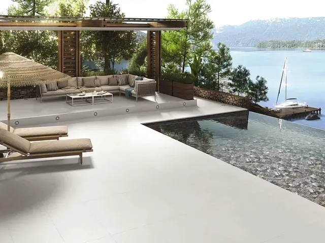 Patio exterior con piscina infinita con vistas a una bahía con yate. Zona de descanso, tumbonas y pérgola.