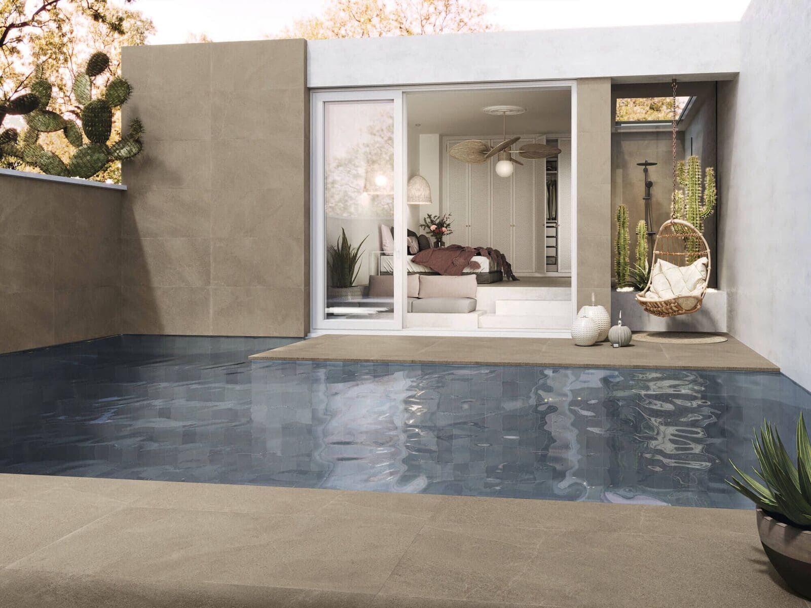 Vista de la piscina desde un dormitorio con puertas corredizas. El agua refleja la habitación abierta y las paredes de estuco, cactus y plantas que la rodean.