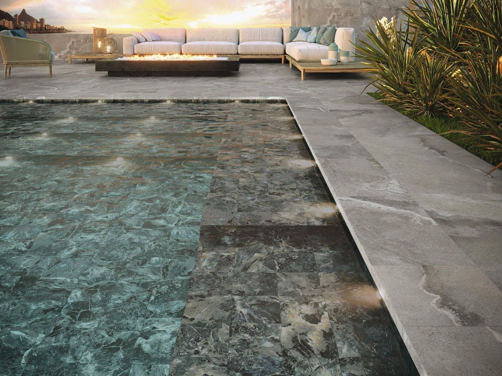 Piscina y patio con fogata, sofá y vegetación al atardecer.