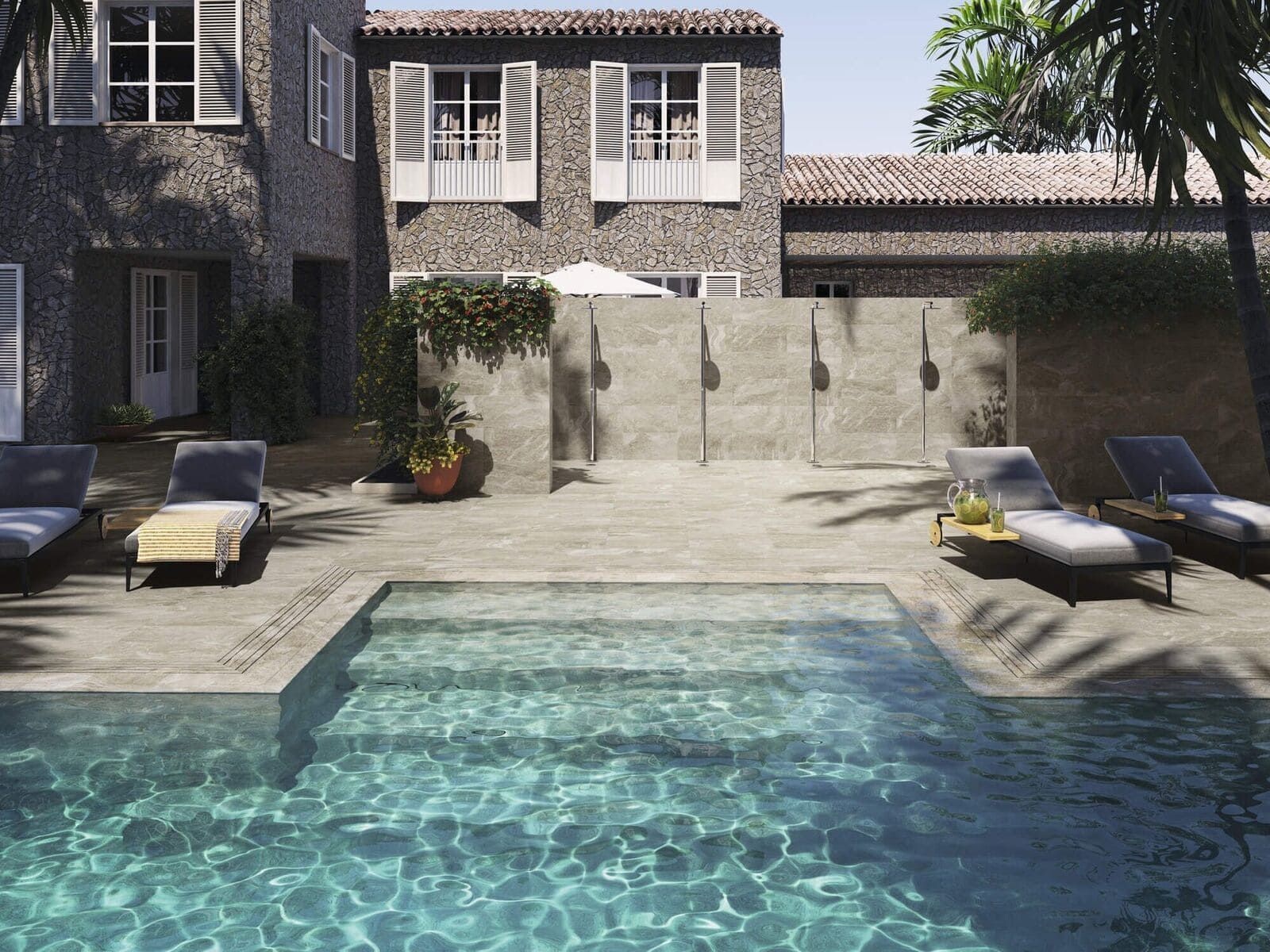 Escena junto a la piscina con un edificio de piedra, tumbonas y una piscina.