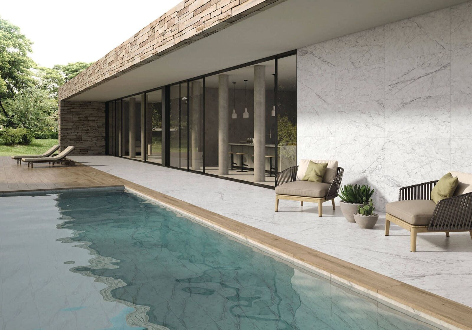 Patio junto a la piscina con sillas modernas, frente a la piscina. Grandes ventanales, muro de piedra y árboles.