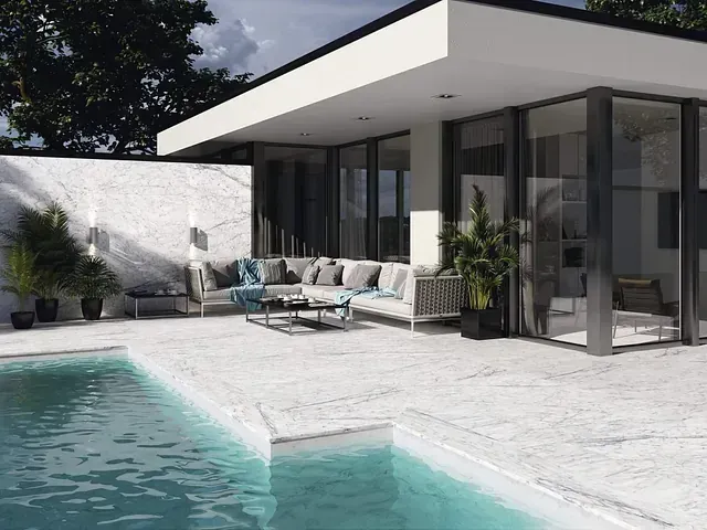 Patio de casa moderna con piscina; diseño de piedra blanca y vidrio con muebles de exterior y plantas.