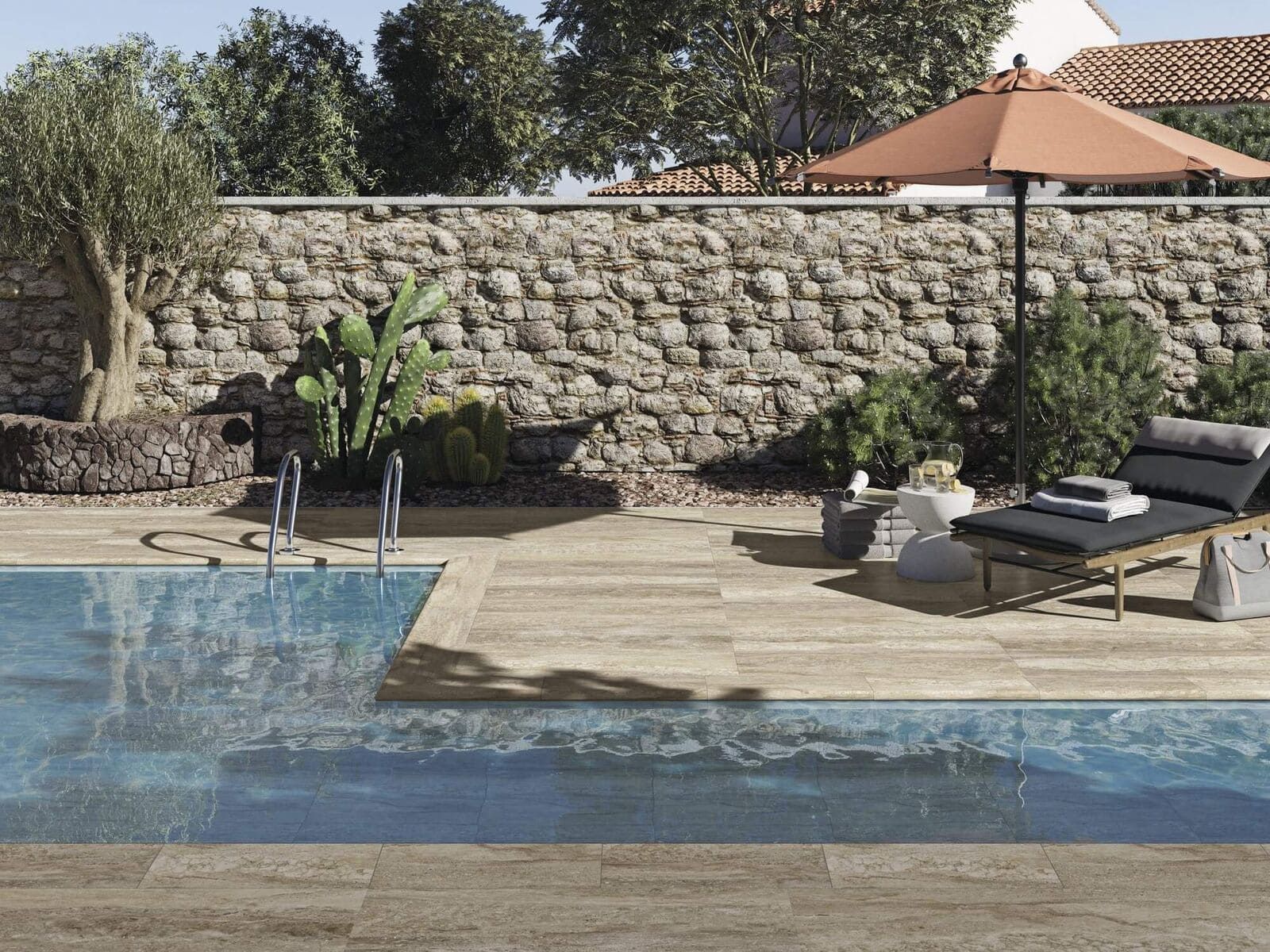 Escena junto a la piscina con muro de piedra, árboles, piscina, tumbona y sombrilla.
