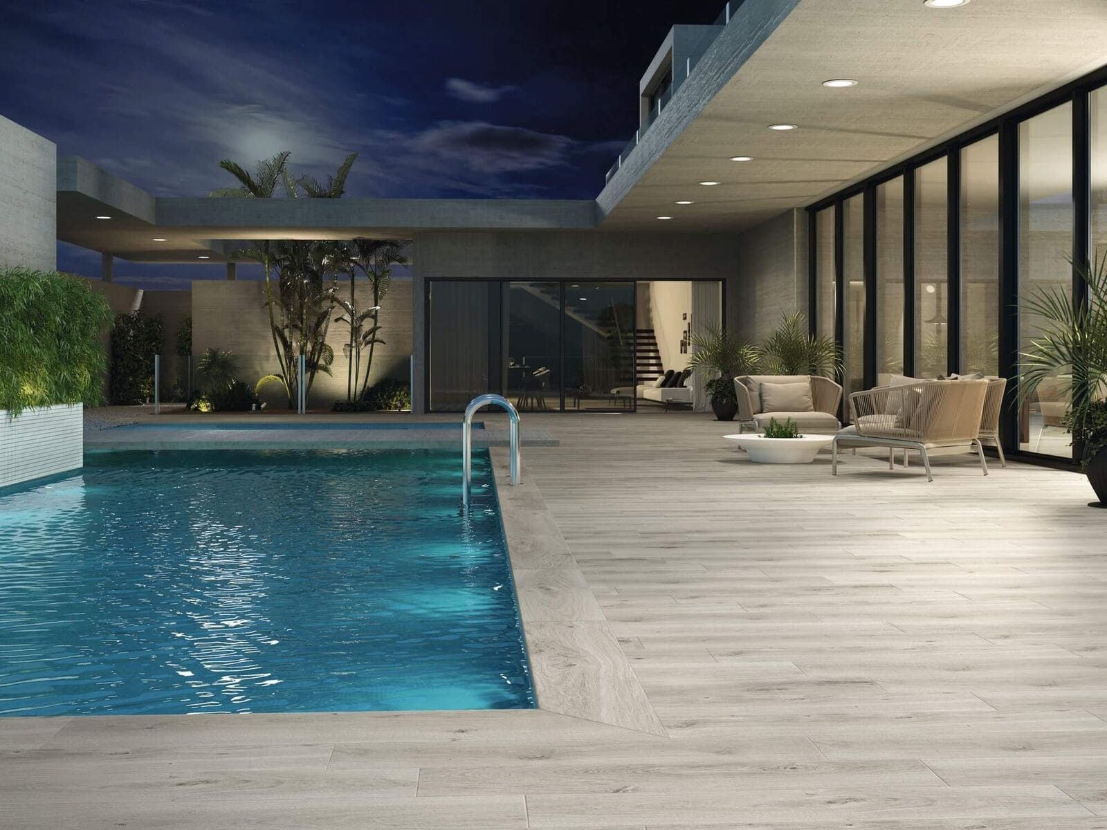 Escena nocturna de una piscina al aire libre, patio de madera con azulejos, muebles de salón debajo de un área cubierta e iluminado por luces de la piscina.